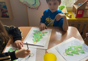 Chłopiec pozuje z choinką, którą maluje farbami